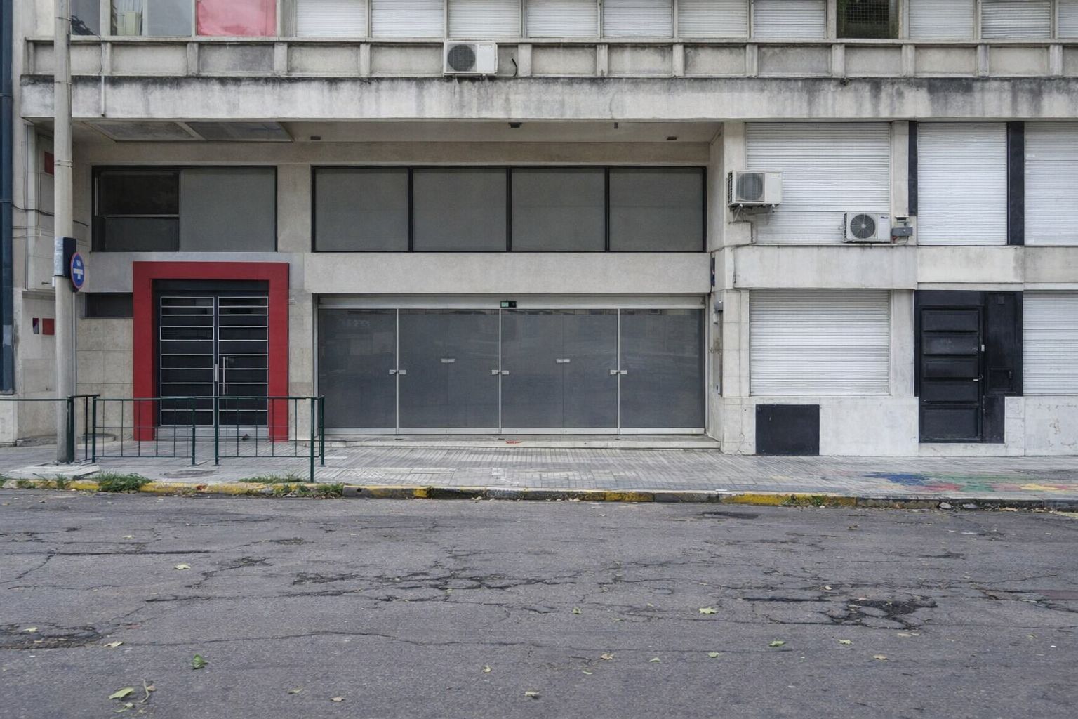 Stängd industrilokal med röd dörrkarm vid en gata.