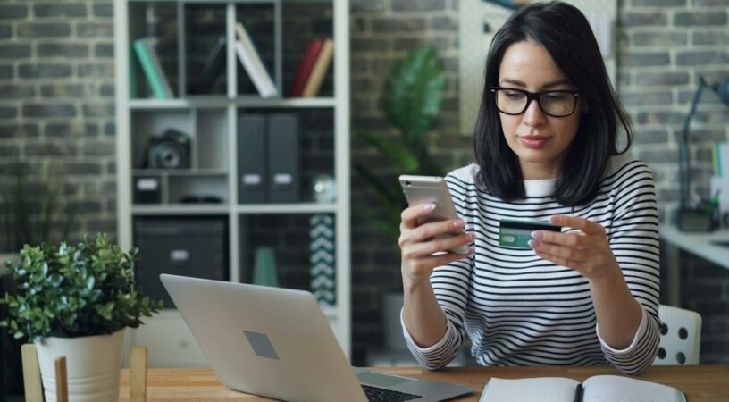 Kvinna granskar ett betalkort och en mobil framför en laptop
